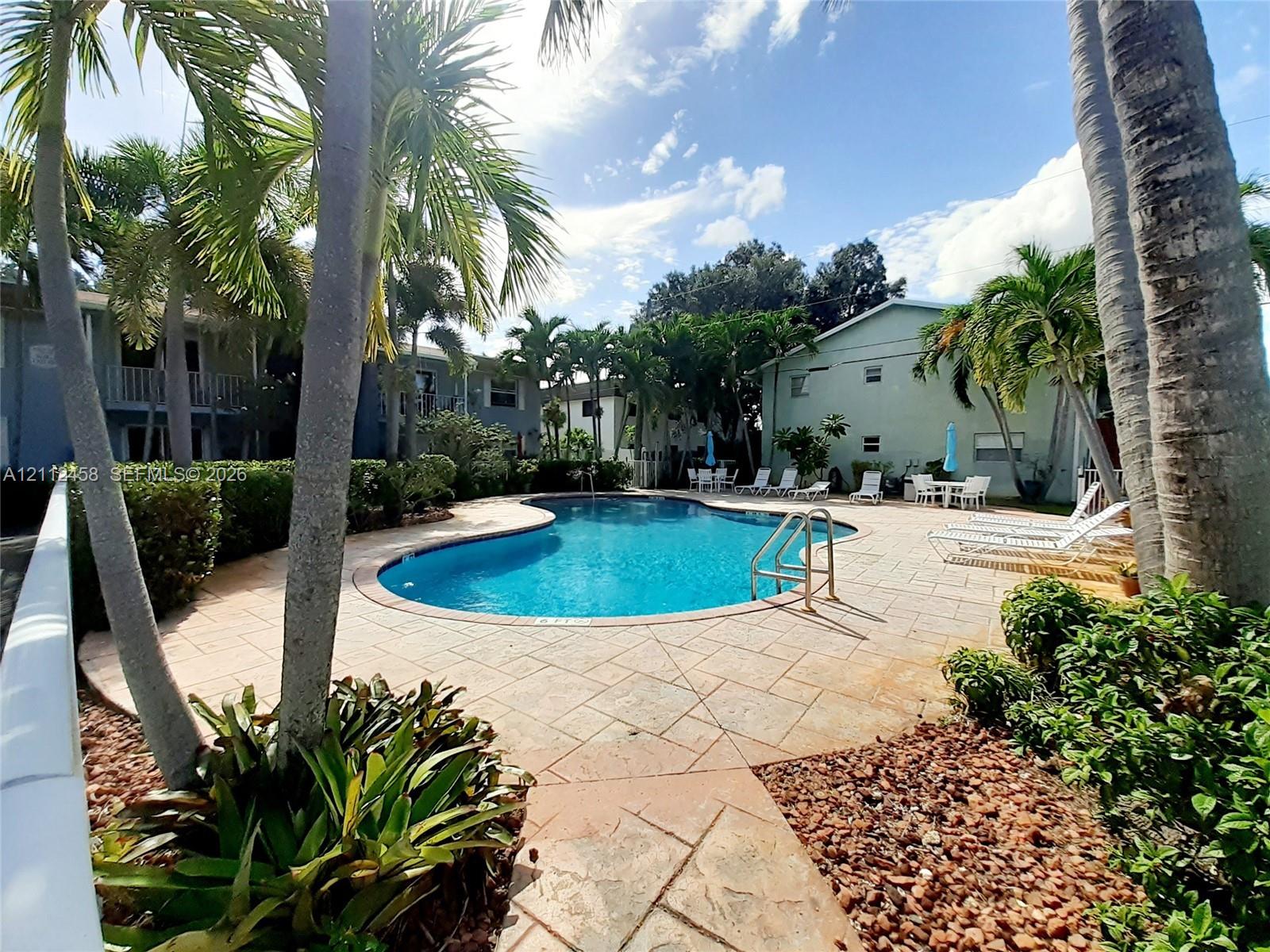 Swimming pool featuring a stone-paver deck, metal pool ladder, mature palm trees, and landscaped shrubbery