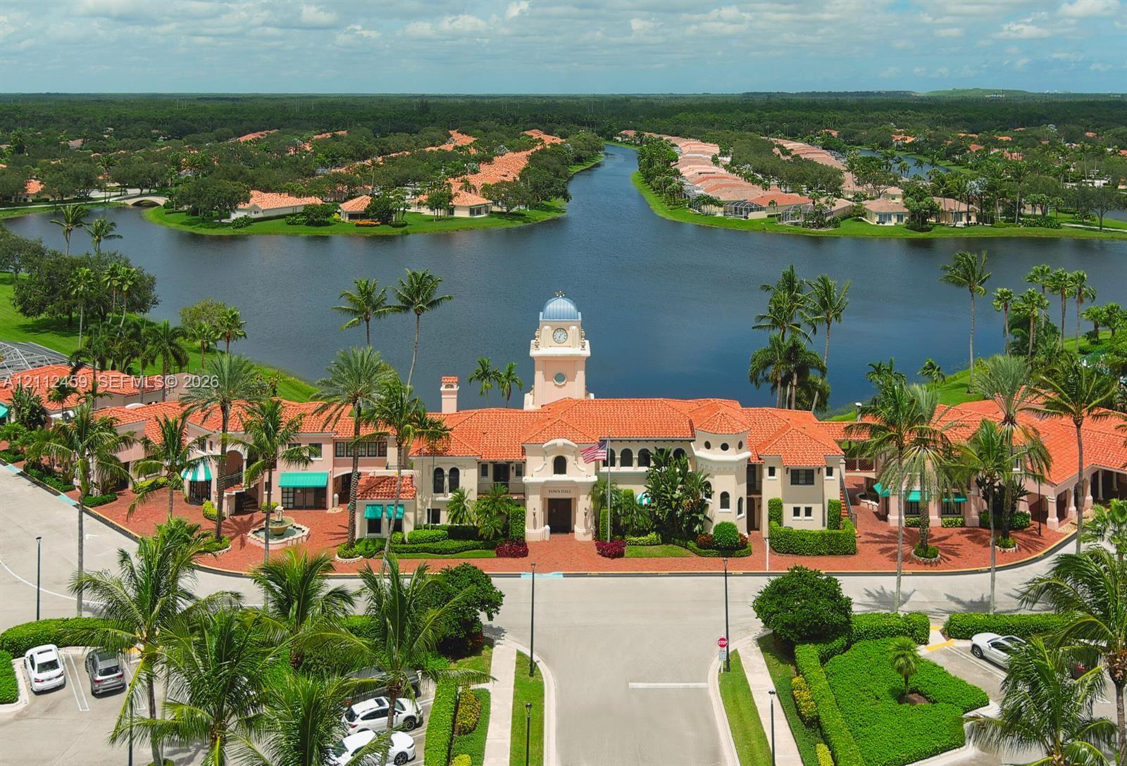Mediterranean-style clubhouse featuring a central clock tower, terracotta tile roofing, stucco exterior, expansive water frontage, and brick-paved entryways