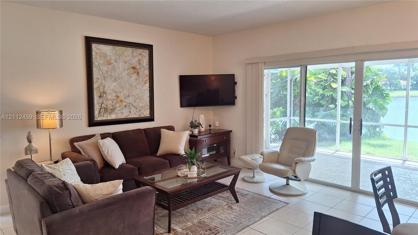 Living area featuring large-format ceramic tile flooring and floor-to-ceiling sliding glass doors opening to a screened lanai with water scenery