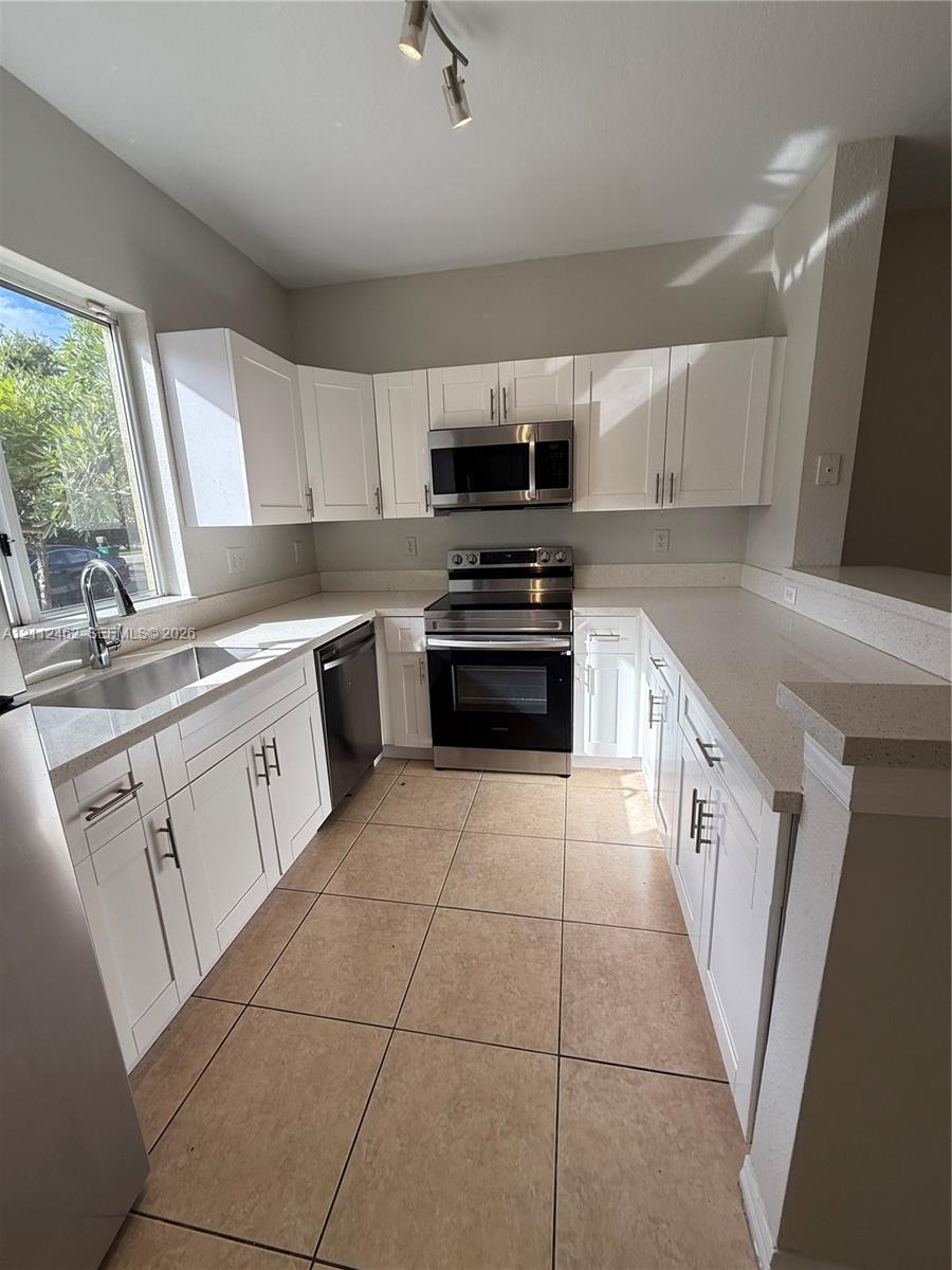 Kitchen featuring white shaker-style cabinetry, stainless steel appliances, neutral countertops, tile flooring, and a single-basin undermount sink