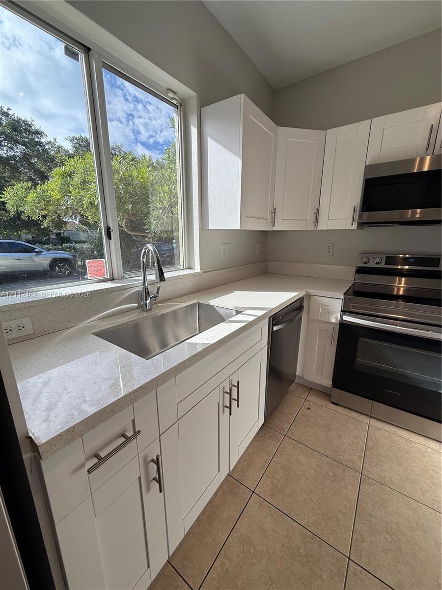 Kitchen featuring white shaker-style cabinetry, stainless steel appliances, quartz countertops, an undermount sink with a gooseneck faucet, and tile flooring