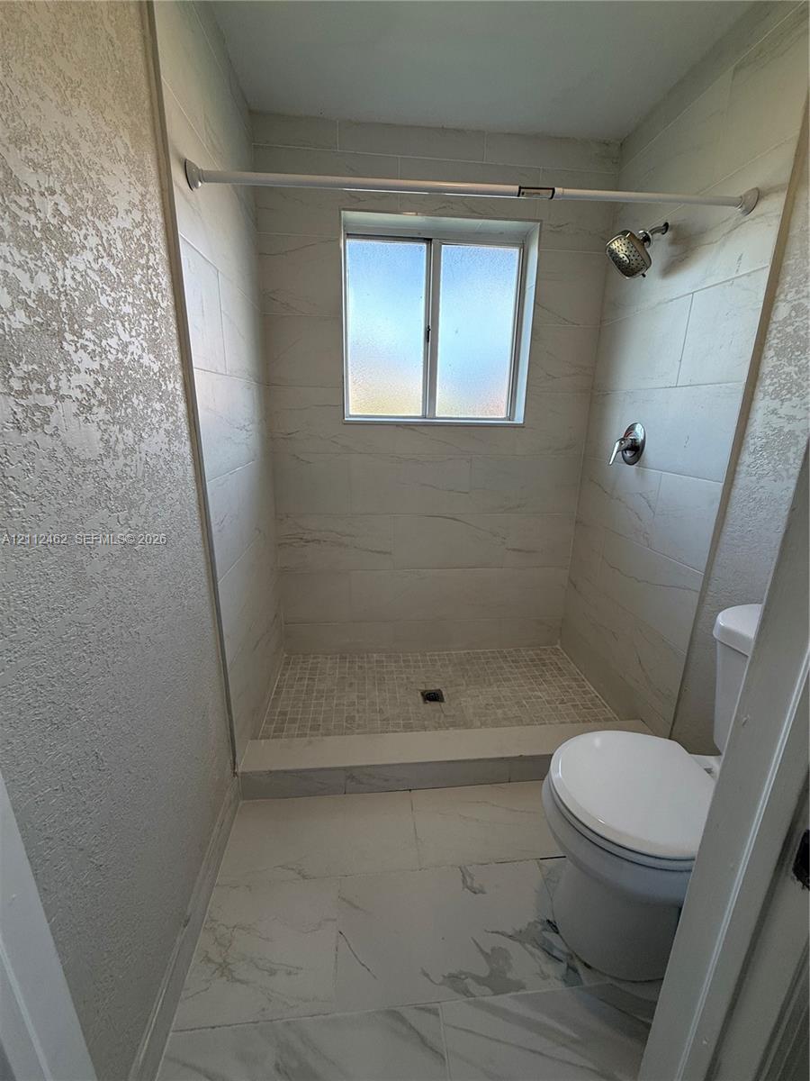 Bathroom featuring large-format tile flooring, a walk-in shower with floor-to-ceiling surround tile, a mosaic-tiled shower floor, and a single-handle wall-mounted shower fixture