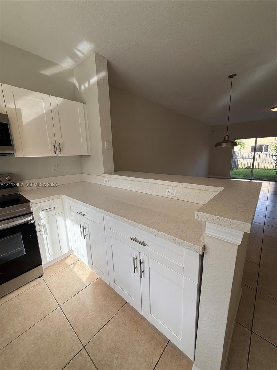 Kitchen featuring white shaker-style cabinetry, neutral stone-composite countertops, stainless steel appliances, ceramic tile flooring, and a breakfast bar