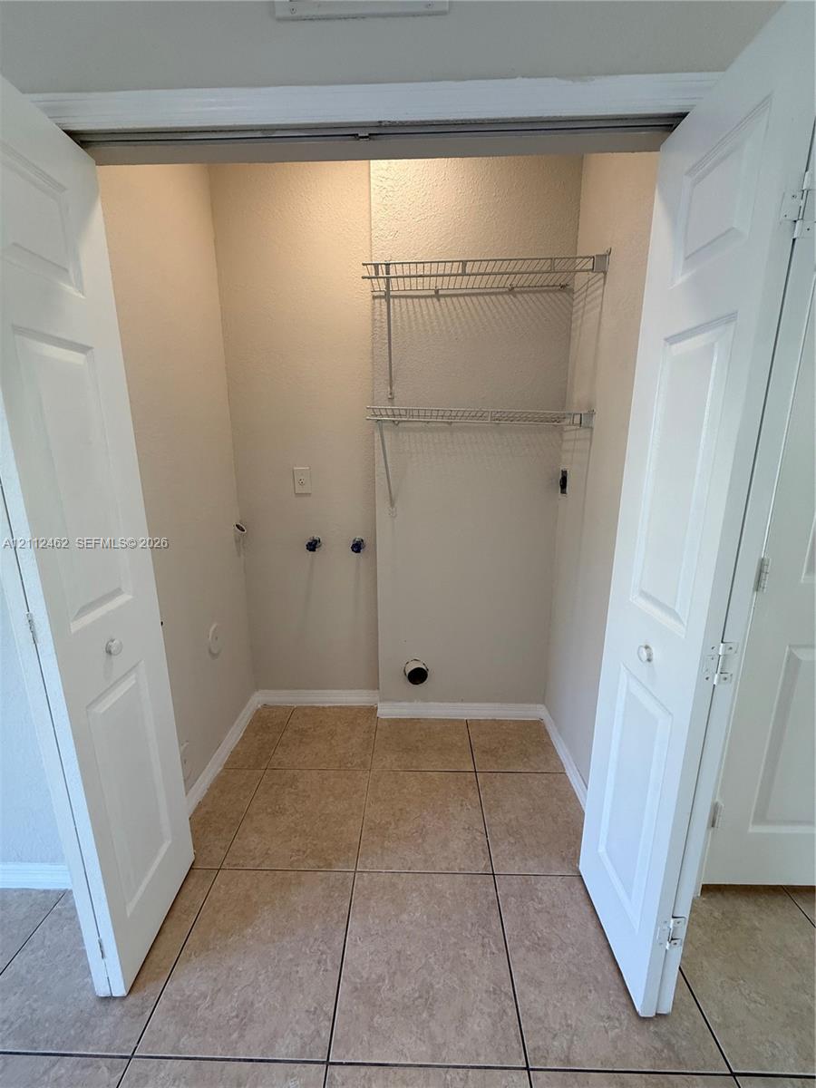 Utility closet featuring dual-folding doors, tile flooring, and integrated metal shelving