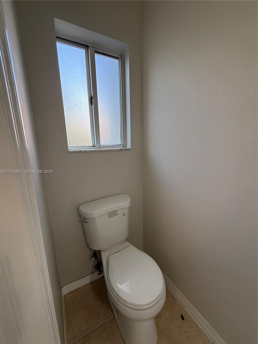 Ceramic tile flooring, white porcelain toilet, and a privacy-glass window with a stone sill