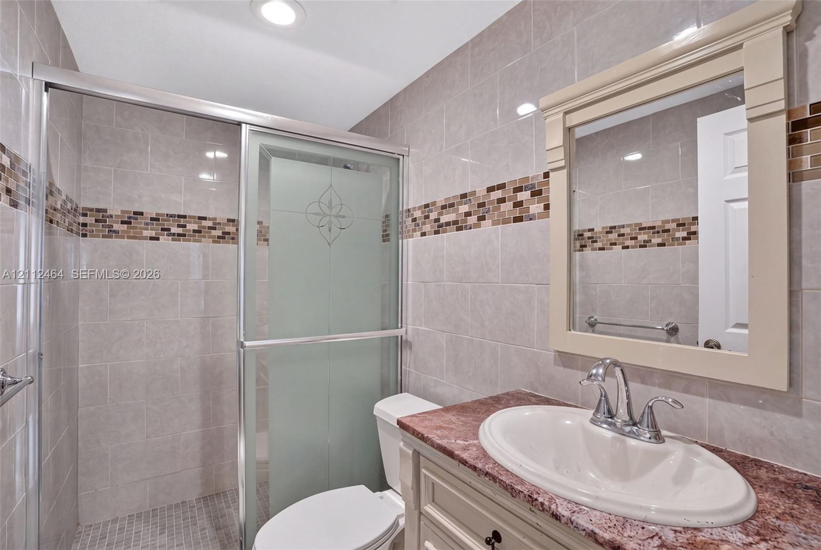 Bathroom featuring a vanity with a stone countertop, an integrated sink, a framed wall mirror, a shower with a sliding glass door, and decorative tile accents