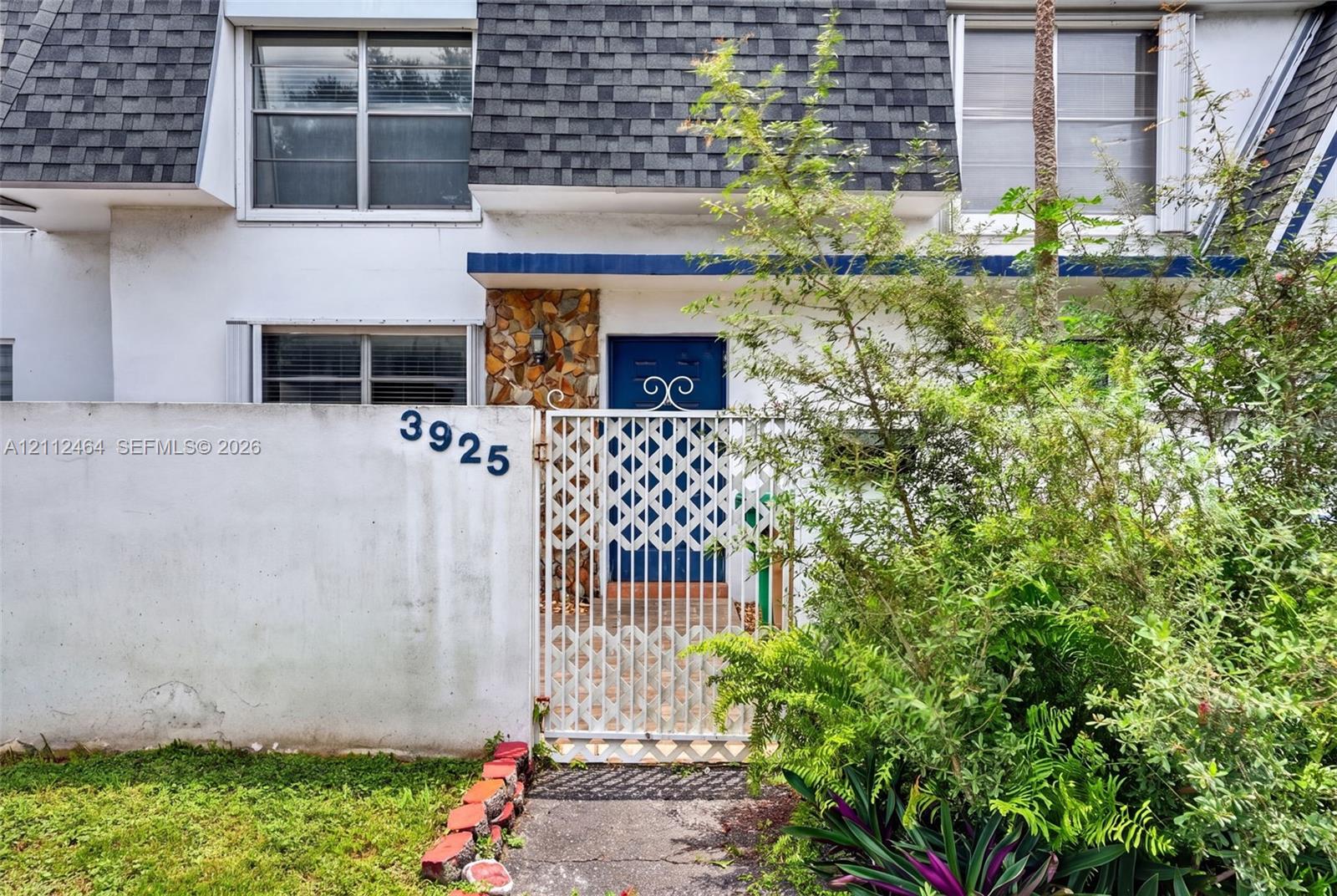 Exterior facade featuring a mansard roof, white stucco wall, stone veneer accent, and a decorative metal gate entry Exterior facade featuring a mansard roof, white stucco wall, stone veneer accent, and a decorative metal gate entry