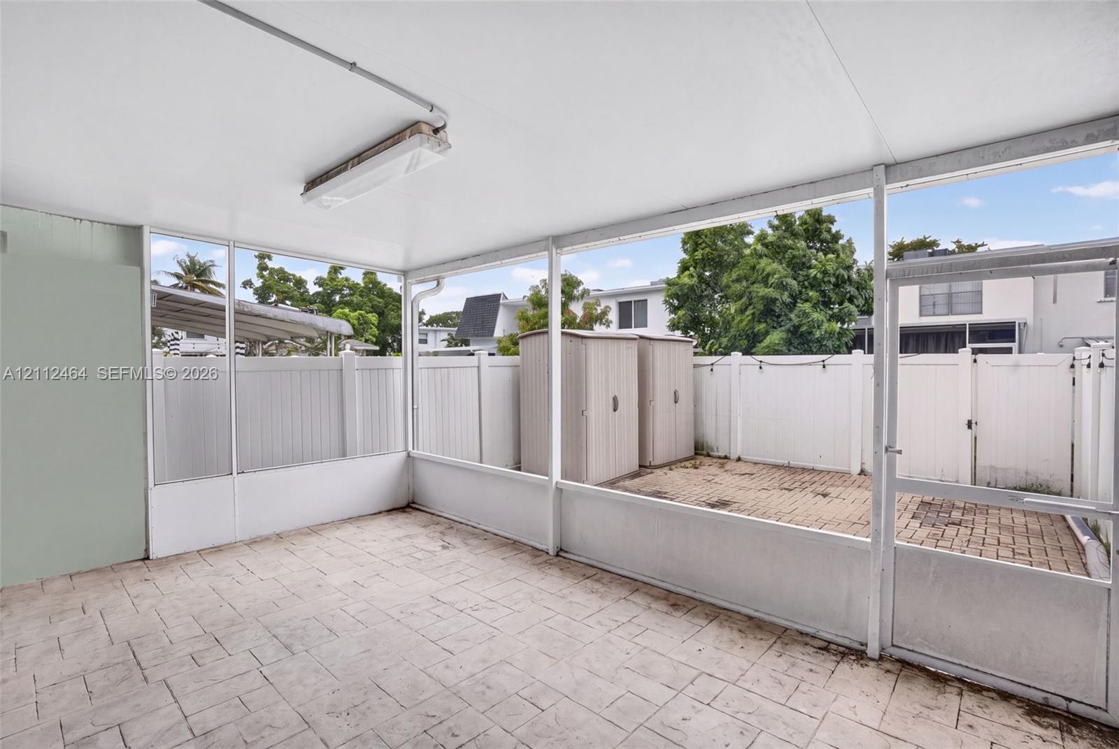 Screened-in patio featuring stamped concrete flooring, overhead lighting, and white privacy fencing