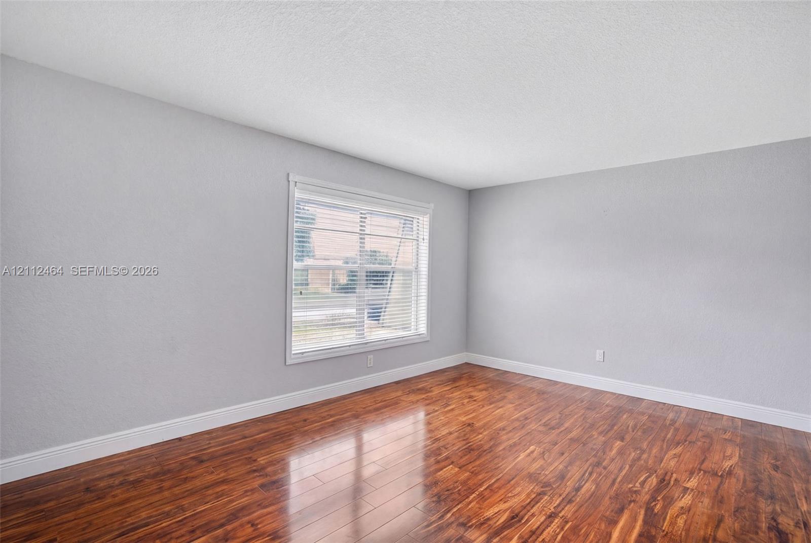 Neutral-toned interior space featuring wood-finish flooring and a single-pane window with white trim