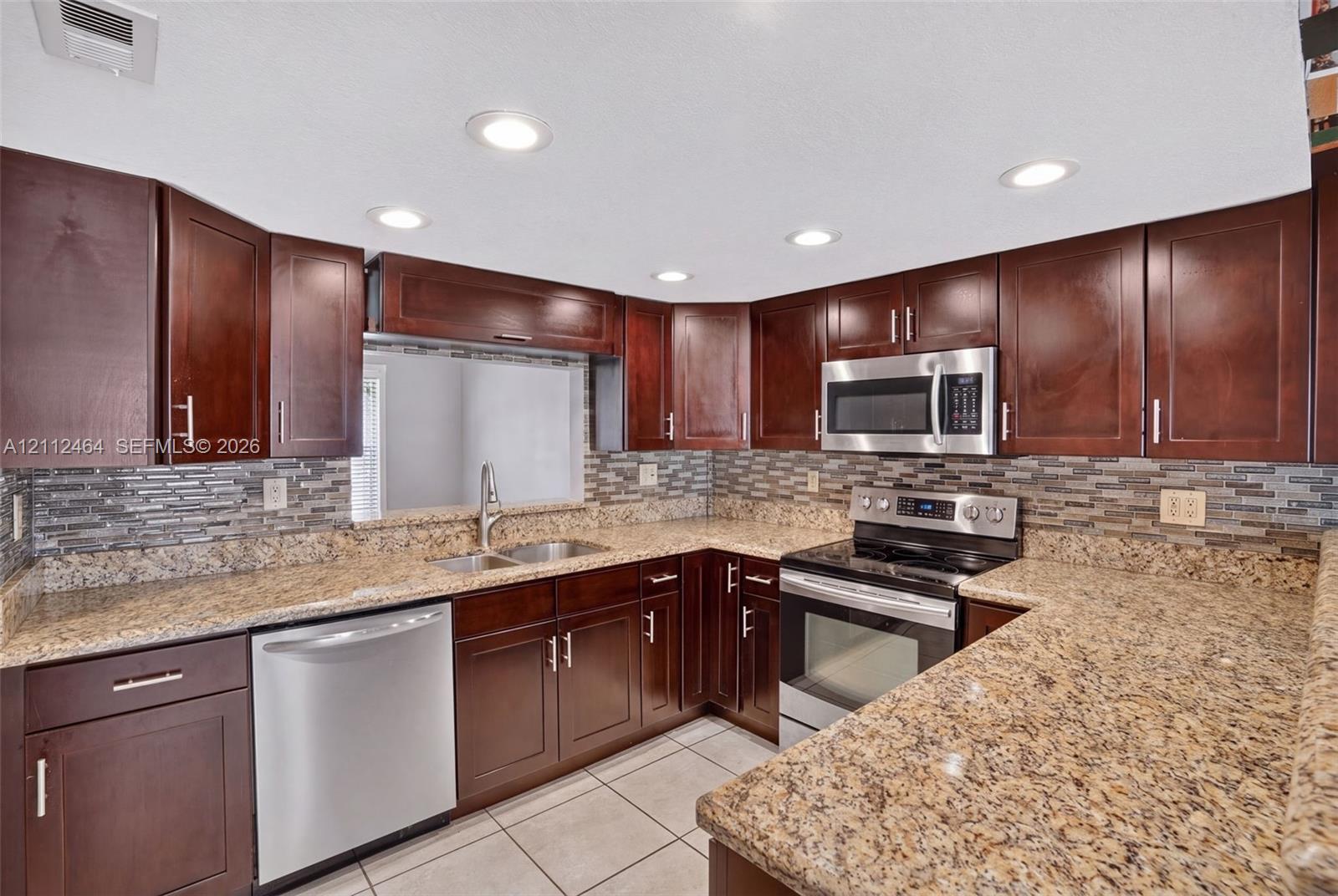 Kitchen featuring dark wood cabinetry, expansive stone-finish countertops, stainless steel appliances, a multi-tonal tiled backsplash, and recessed ceiling lighting