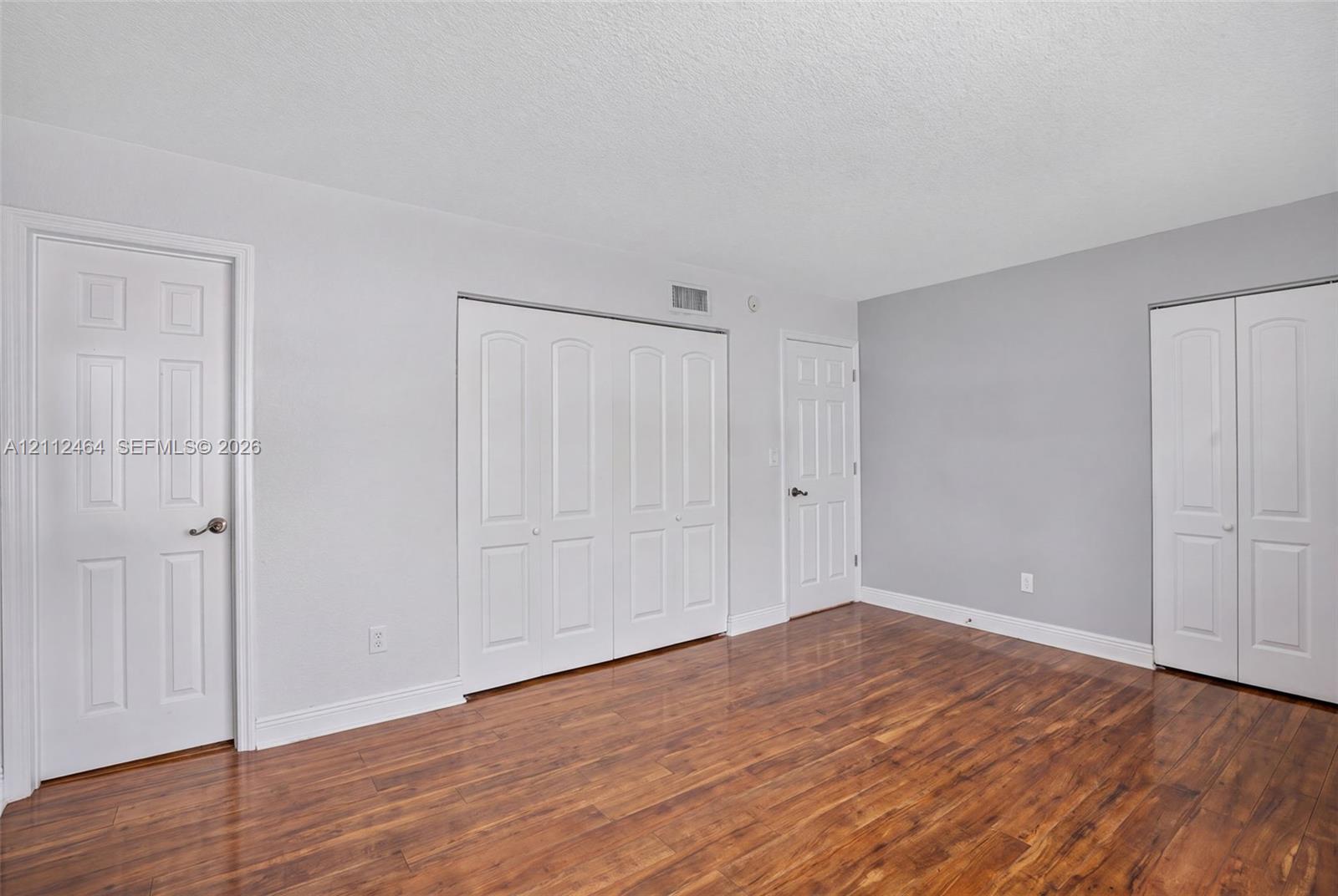 Room featuring wood-finish flooring, neutral walls, two sets of white bifold closet doors, and two interior doors with satin nickel hardware