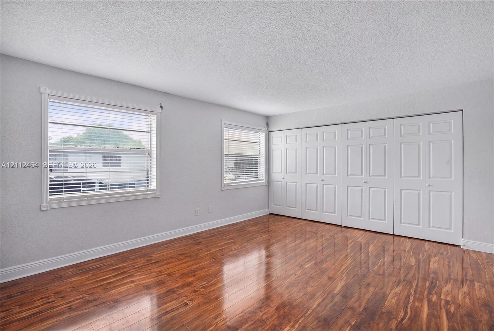 Wood-finish flooring, two large windows with horizontal blinds, and a set of multi-panel bi-fold closet doors