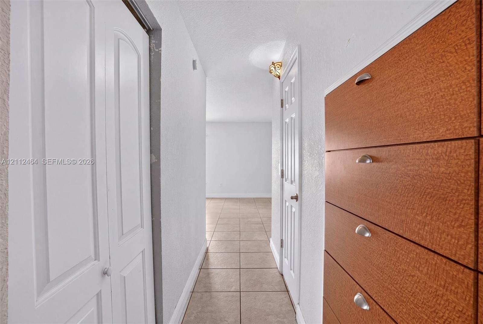 Hallway featuring ceramic tile flooring, built-in wooden cabinetry with metal hardware, and multi-panel interior doors Hallway featuring ceramic tile flooring, built-in wooden cabinetry with metal hardware, and multi-panel interior doors