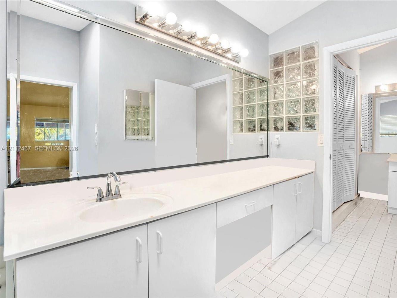 Extended vanity featuring a smooth surface countertop, integrated oval sink, full-width wall mirror, chrome-finish faucet, and privacy glass block window