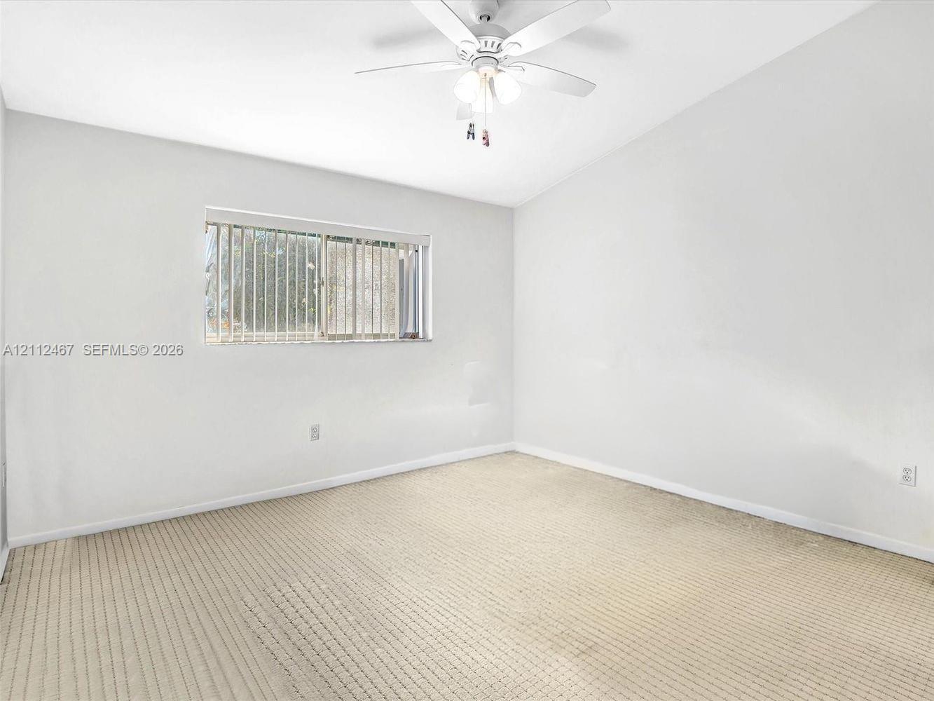 Neutral interior featuring carpeting, a vaulted ceiling, and a ceiling-mounted light fixture with a fan