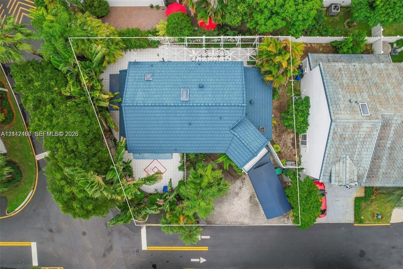 Aerial perspective featuring a tile roof, paved driveway, carport, and landscaped grounds
