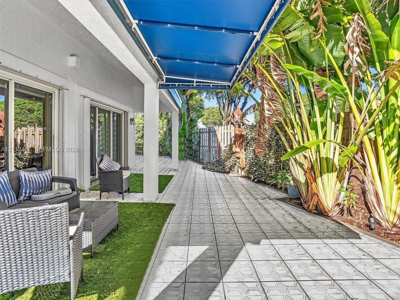 Covered outdoor patio featuring retractable blue fabric awning, patterned tile flooring, and integrated artificial turf sections