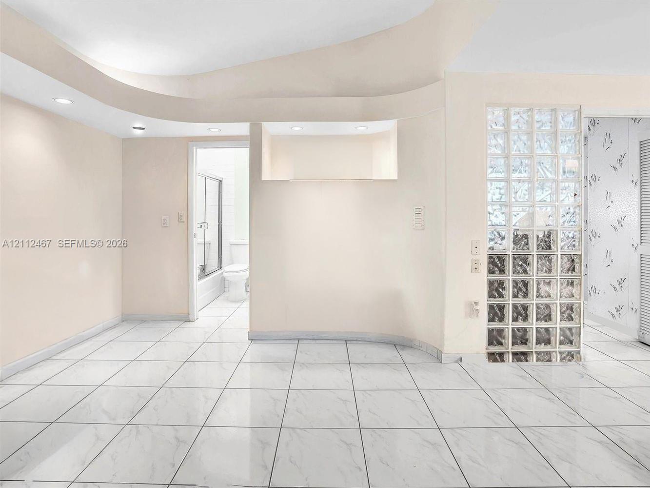 Interior space featuring large-format tile flooring, a curved architectural ceiling detail with recessed lighting, a built-in recessed wall niche, and a decorative glass block partition wall