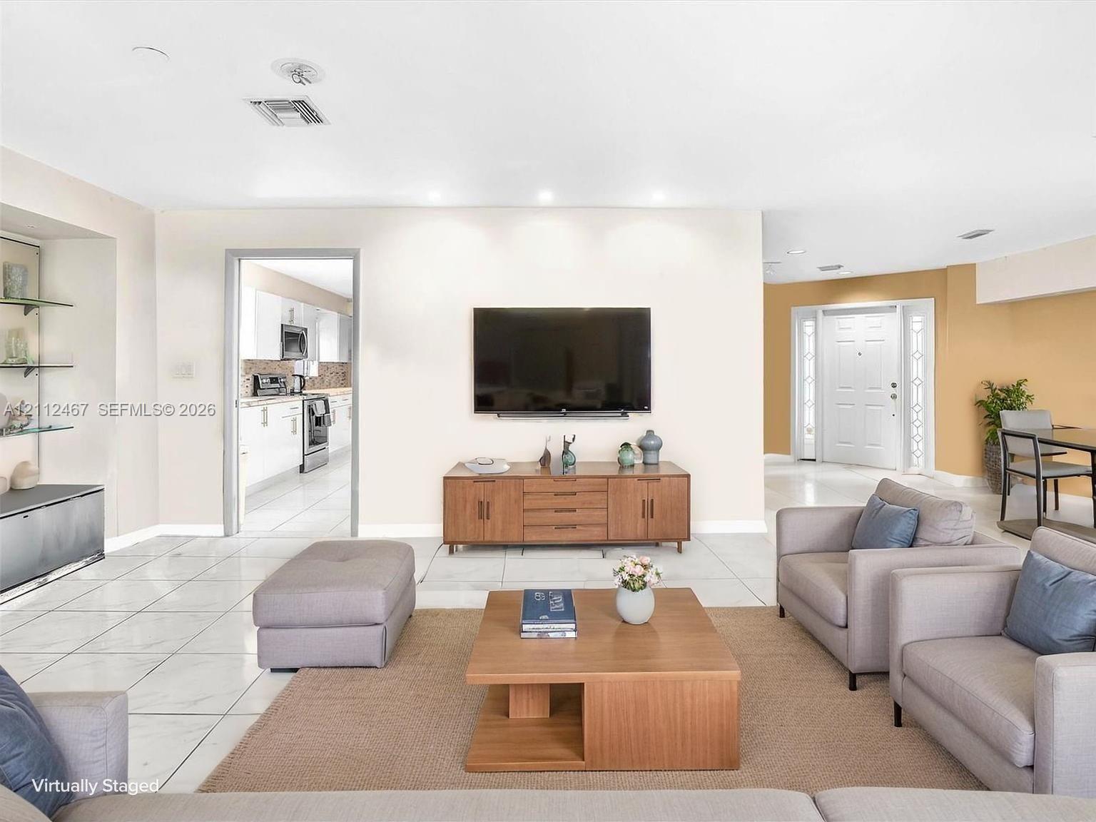 Open-concept living space featuring large-format tile flooring, recessed ceiling lighting, a built-in recessed shelving niche, and a multi-panel exterior entry door with glass side panels