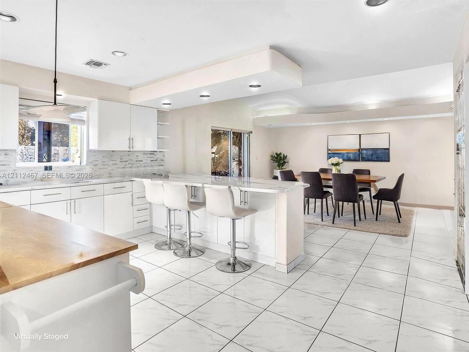 Kitchen featuring white cabinetry, stone-finish countertops, a tiered kitchen island, recessed lighting, and tile flooring