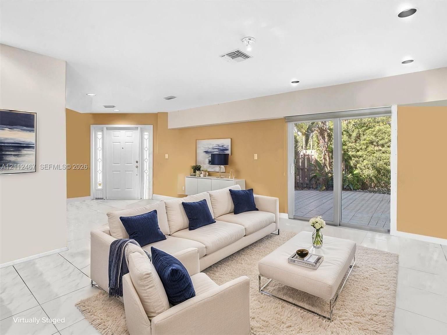 Open-concept interior featuring light-toned tile flooring, recessed ceiling lighting, a multi-panel front door with sidelights, and large glass sliding doors providing exterior deck access