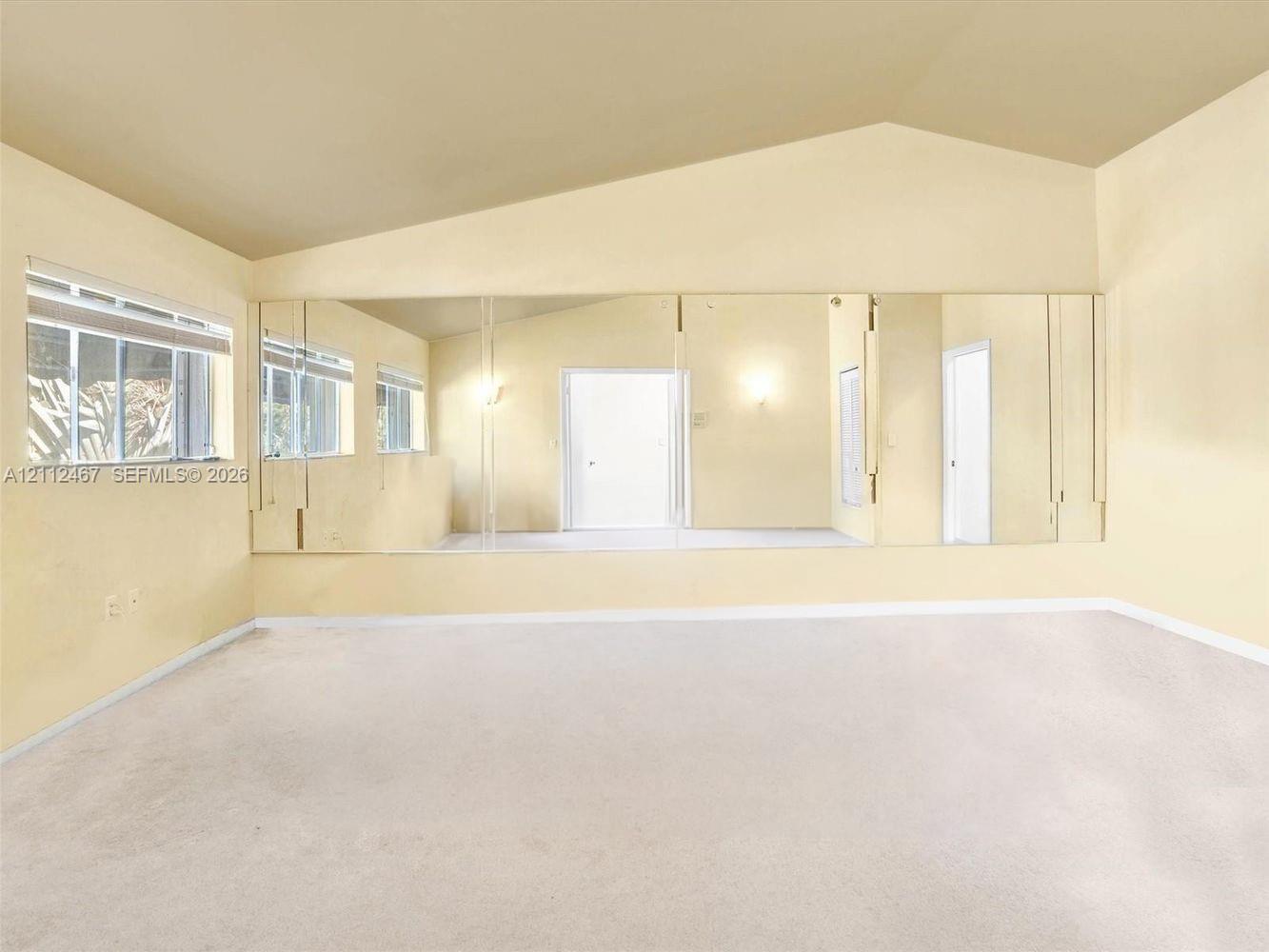 Vaulted ceiling, expansive wall-to-wall mirrored paneling, and carpeted flooring