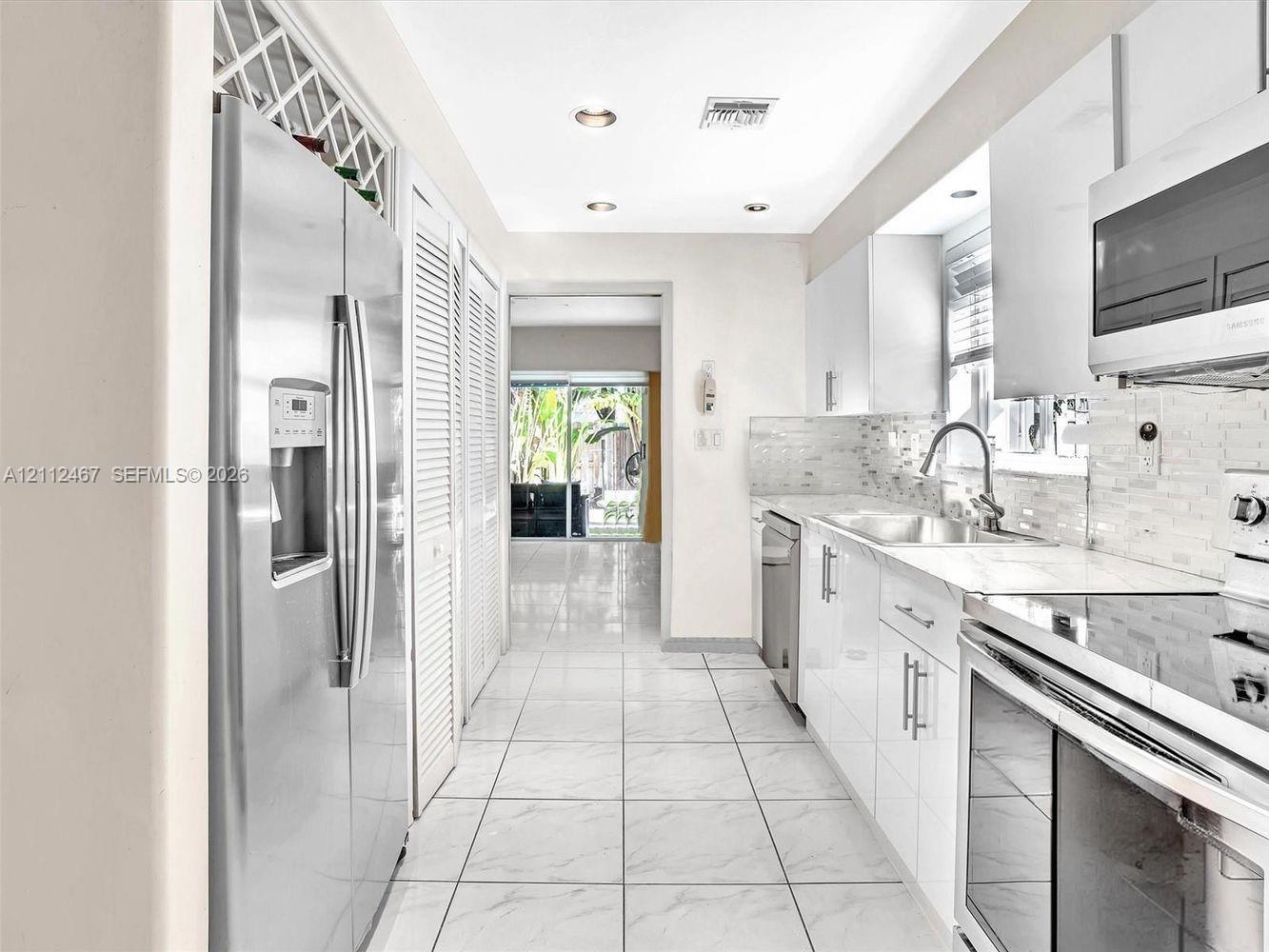 Galley kitchen featuring high-gloss cabinetry, stainless steel appliances, a mosaic tile backsplash, and tile flooring