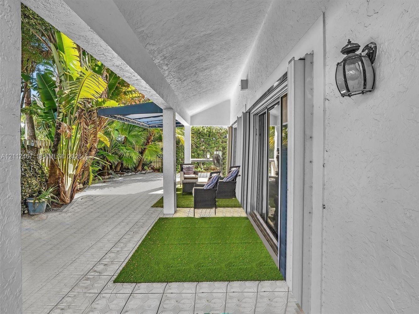 Covered patio featuring textured stucco exterior walls, light-toned paved flooring, an attached wall-mounted lantern light fixture, and floor-to-ceiling glass sliding doors