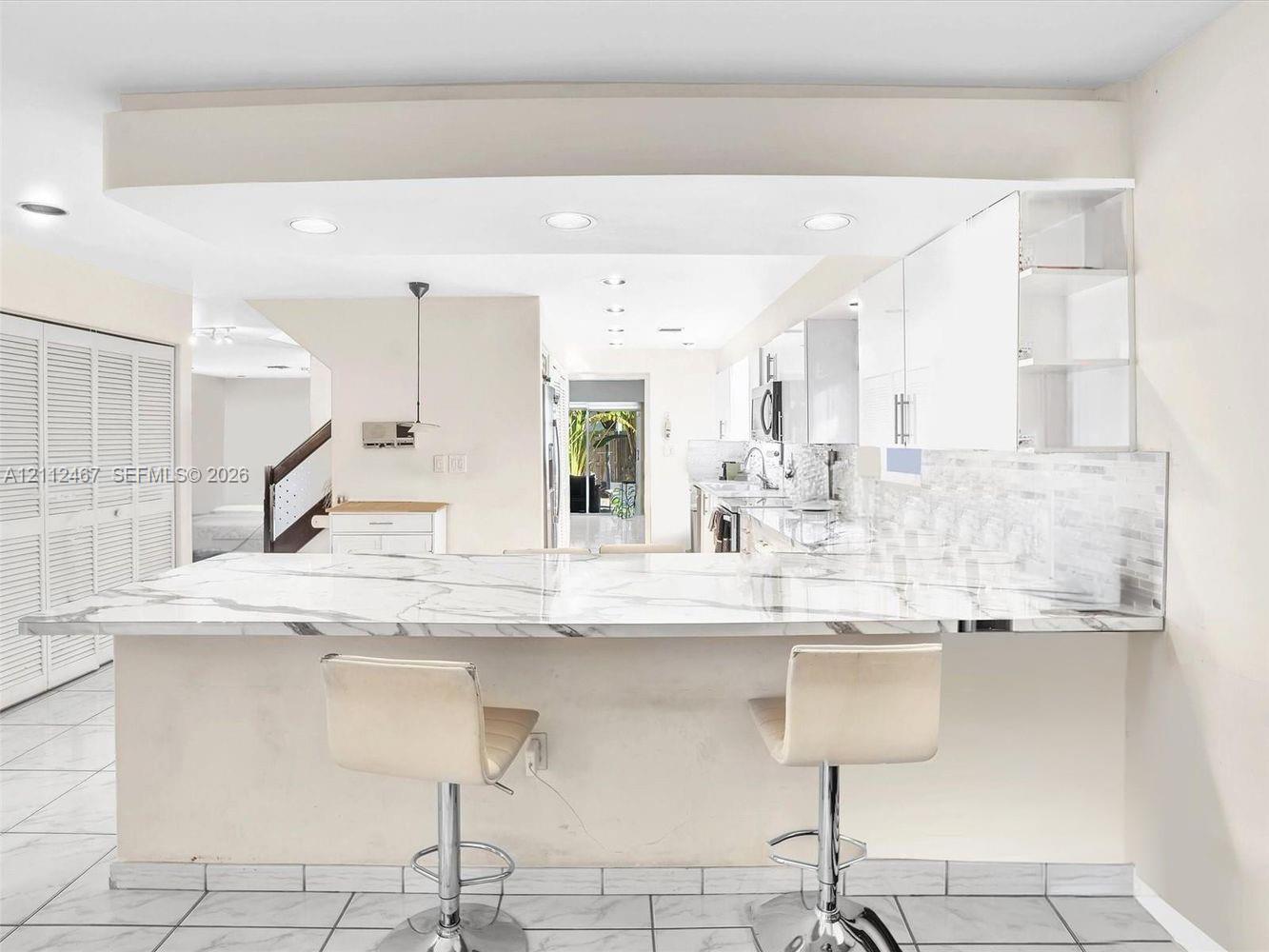 Kitchen featuring a stone-surface breakfast bar, white flat-panel cabinetry, tiled backsplash, recessed lighting, and tile flooring