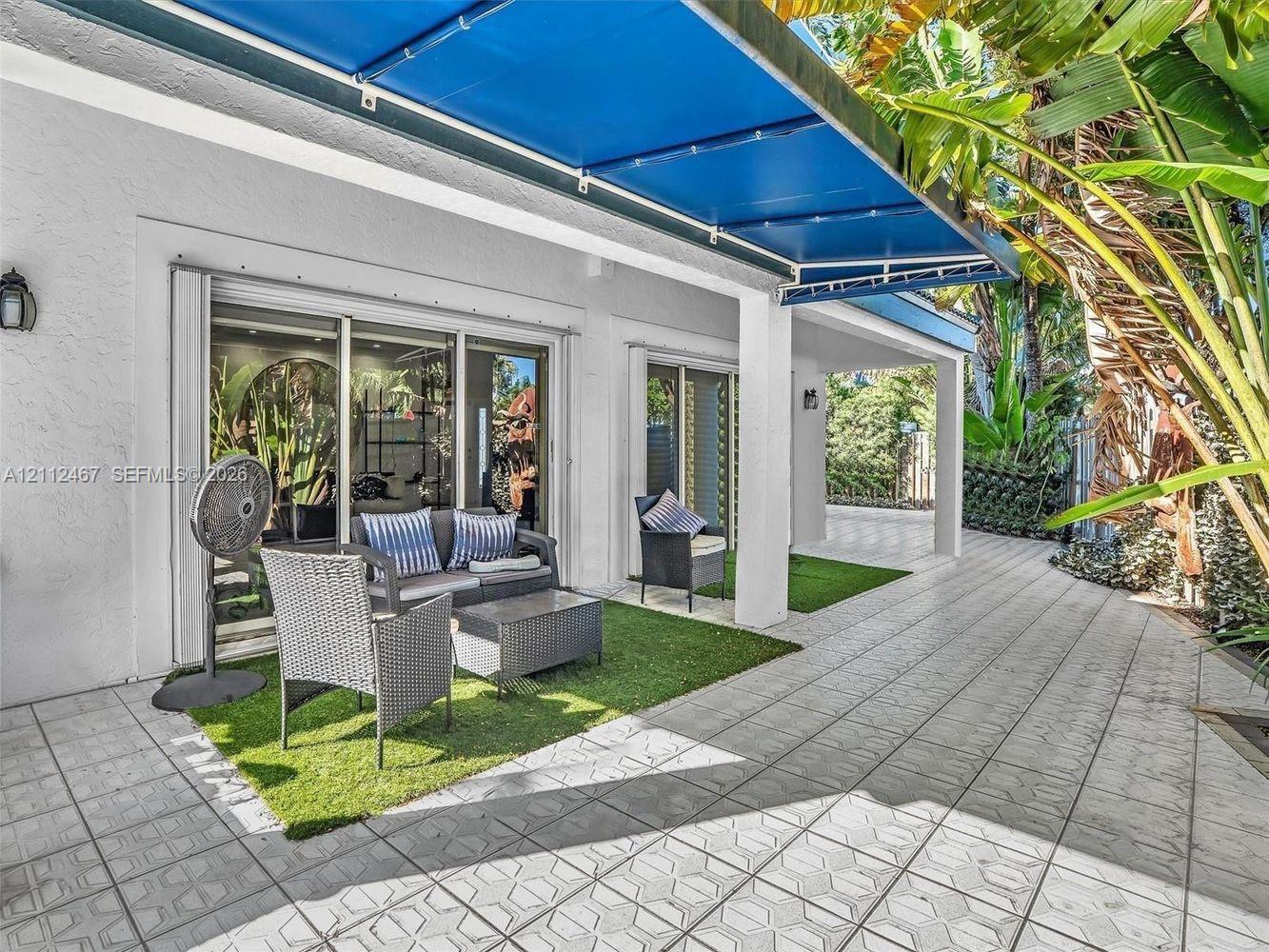 Covered patio featuring patterned tile flooring, retractable blue fabric awning, and recessed sliding glass doors