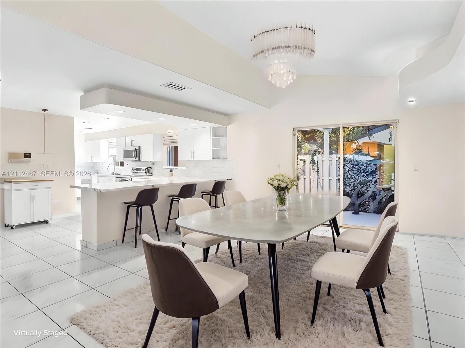 Open-concept kitchen featuring white cabinetry, a spacious breakfast bar, multi-tiered tiered chandelier lighting, and large-format tile flooring