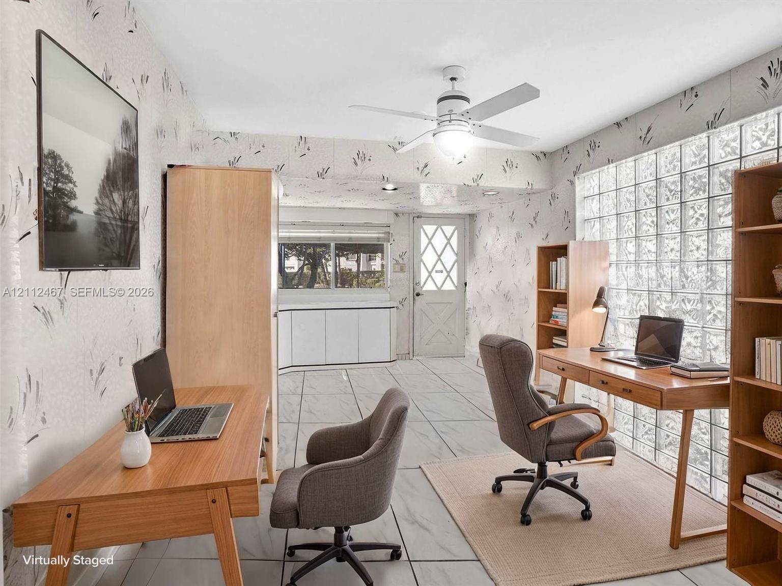 Room featuring light-toned tile flooring, a grid-patterned glass block wall, and a ceiling fan with integrated lighting