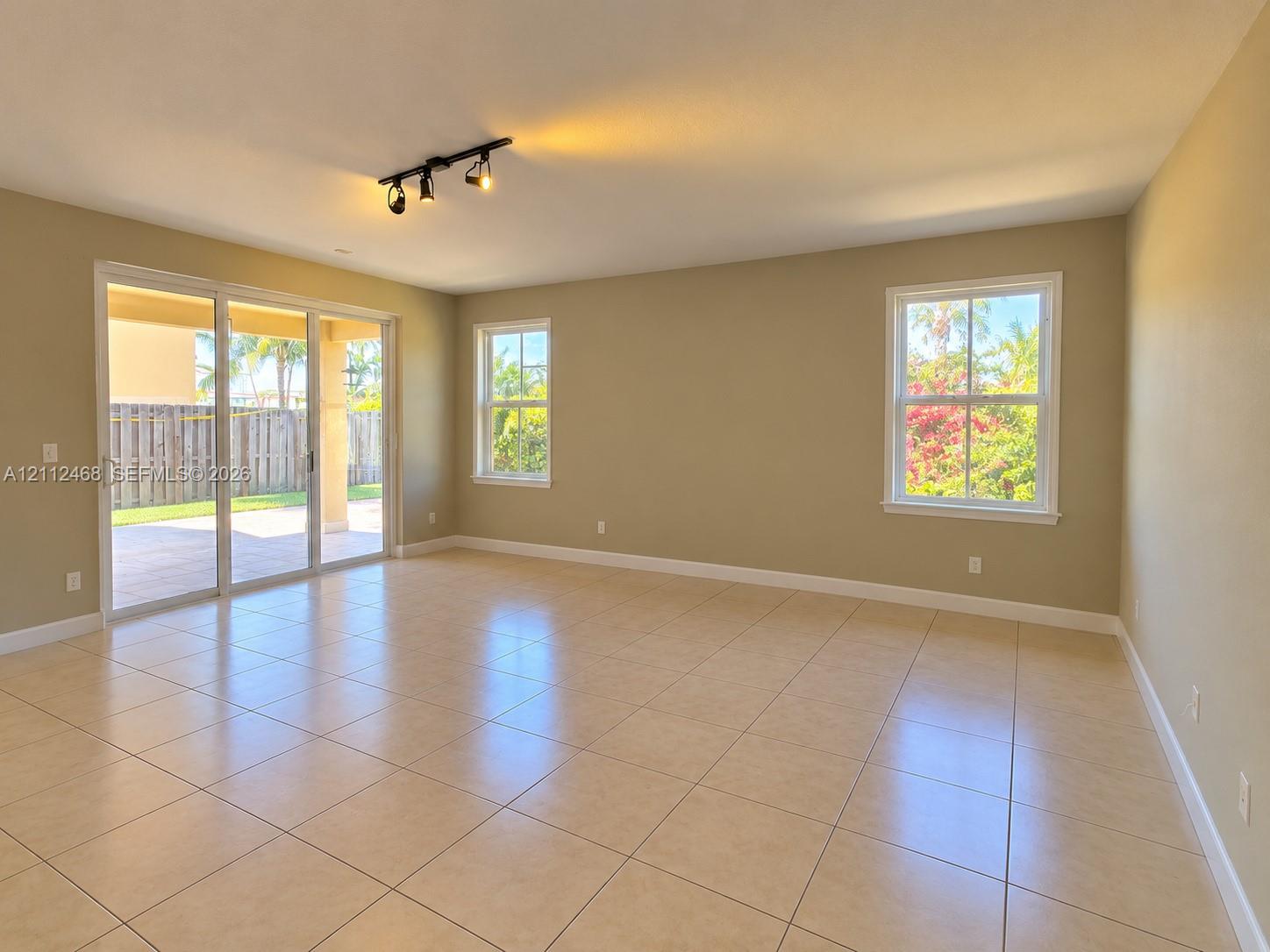 Open-concept interior featuring neutral tile flooring, multi-panel sliding glass doors, multi-pane windows, and a three-light track lighting fixture