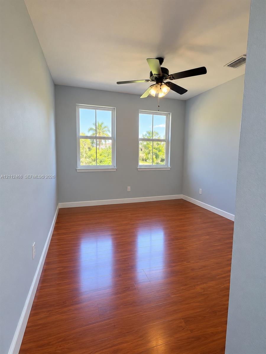 Room featuring wood-finish flooring, dual windows with grid detailing, and a multi-light ceiling fan