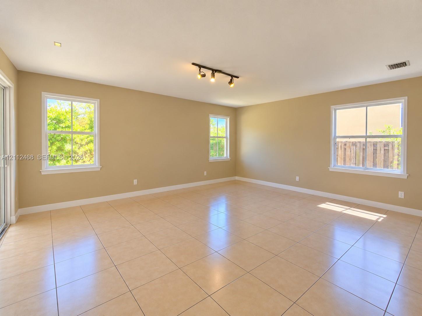 Neutral-toned interior featuring ceramic tile flooring, three multi-pane windows, and a ceiling-mounted track lighting fixture