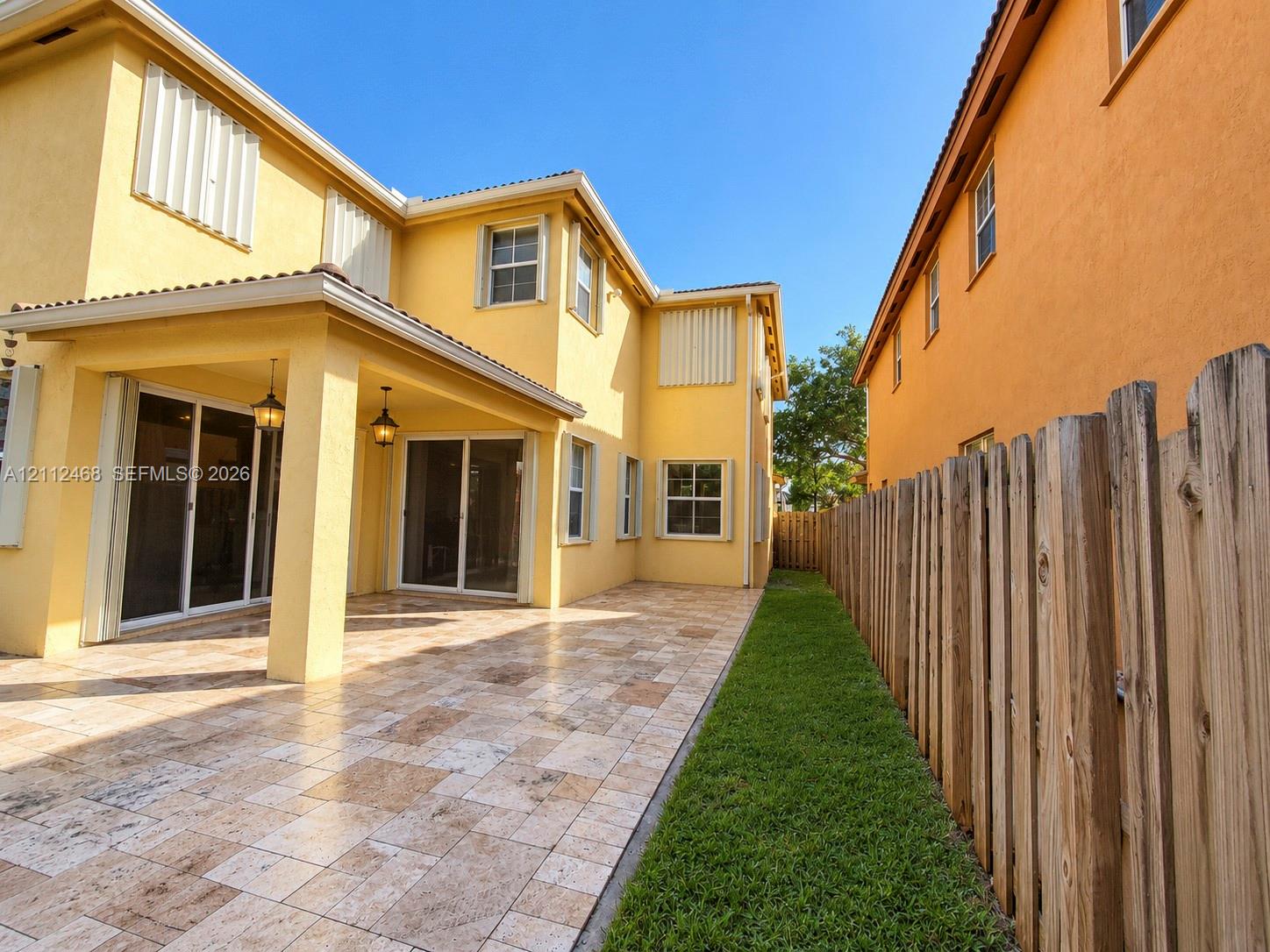 Stucco exterior featuring a covered patio with tile flooring, recessed outdoor lighting, dual sliding glass doors, and a wood-slat perimeter fence