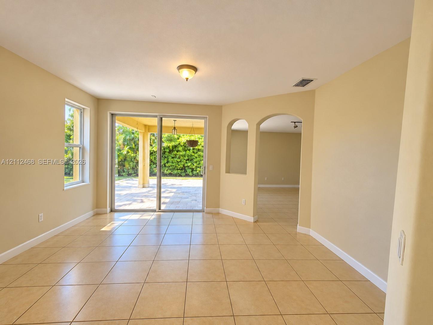 Ceramic tile flooring, arched wall openings, and sliding glass doors opening to a covered patio