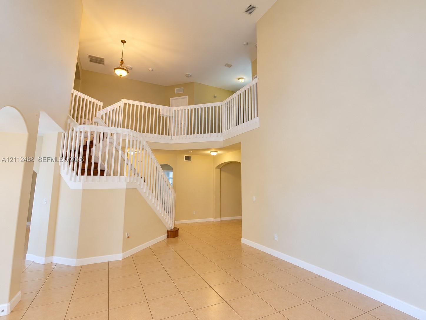 Two-story foyer featuring high ceilings, tile flooring, an open staircase with white balusters, arched entryways, and pendant lighting