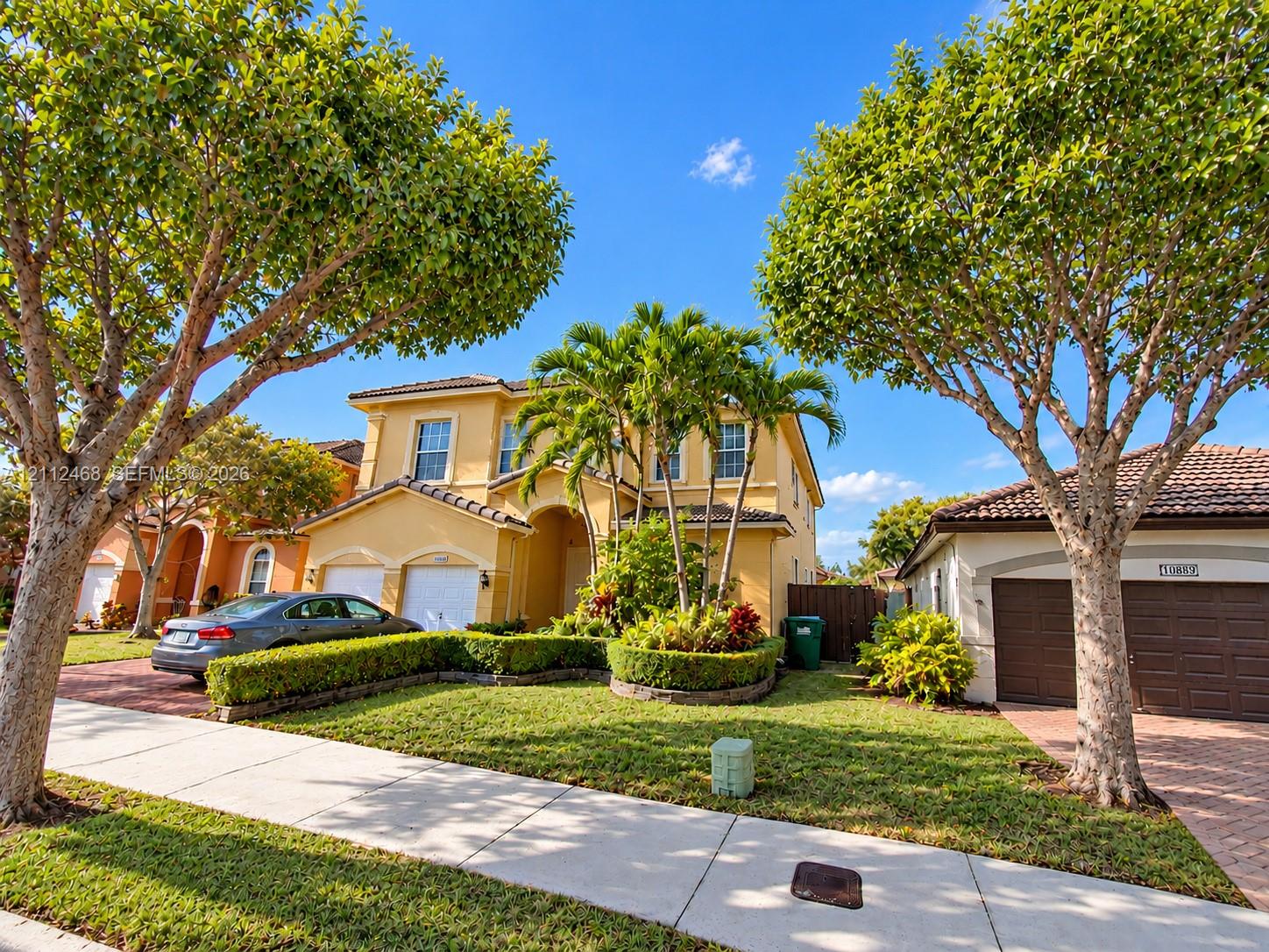 Two-story stucco exterior featuring a multi-gabled tile roof, arched entryway, and integrated two-car garage with brick-paver driveway