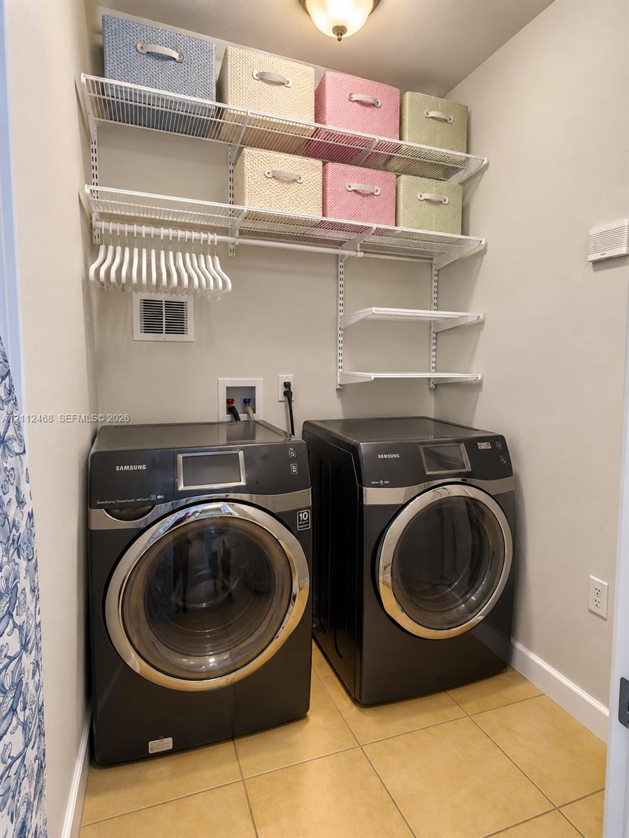 Utility area featuring metal wire shelving, tiled flooring, and dual front-loading appliances