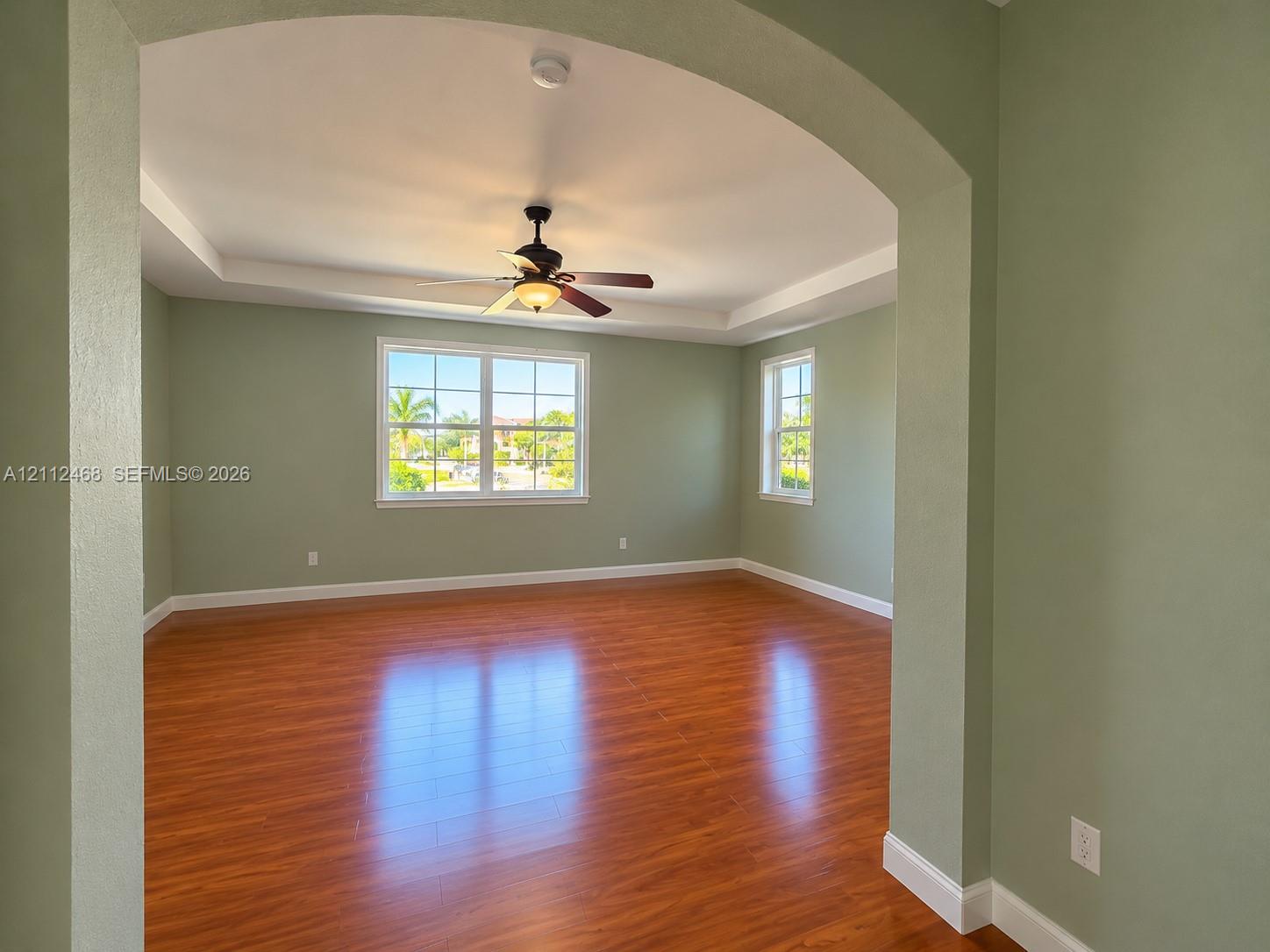 Interior space featuring wood-finish flooring, a tray ceiling with a center-mounted ceiling fan, and multi-lite windows framed by arched doorways