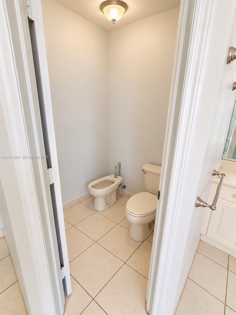 Water closet featuring a two-piece toilet, bidet, neutral tile flooring, and a flush-mount ceiling light fixture