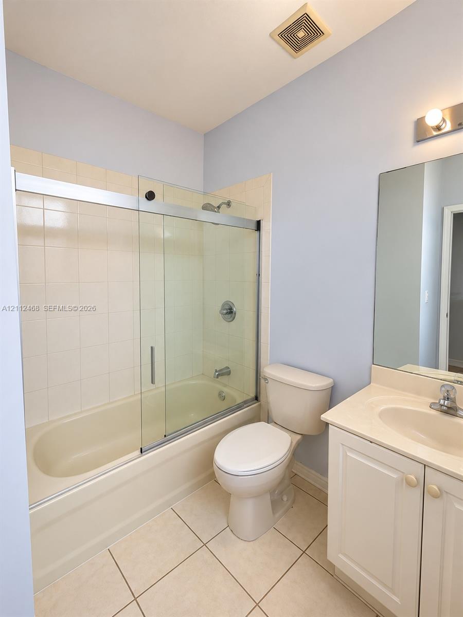 Bathroom featuring a tub-shower combination with glass sliding doors, ceramic tile shower surround, vanity with an integrated sink, and large wall-mounted mirror