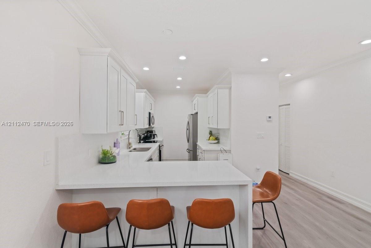 Kitchen featuring white cabinetry, solid-surface countertops, recessed ceiling lighting, and wood-finish flooring