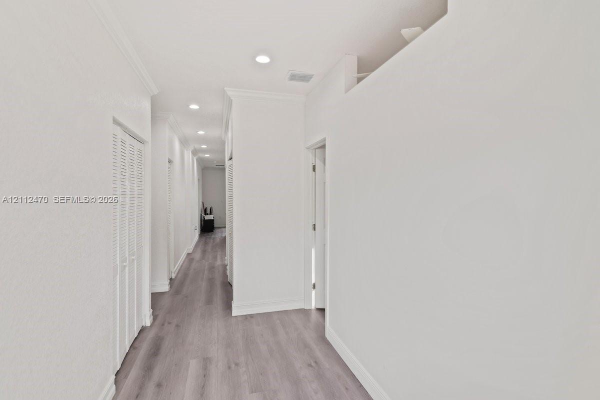 Hallway featuring wood-finish flooring, recessed lighting, and louvered-door closets