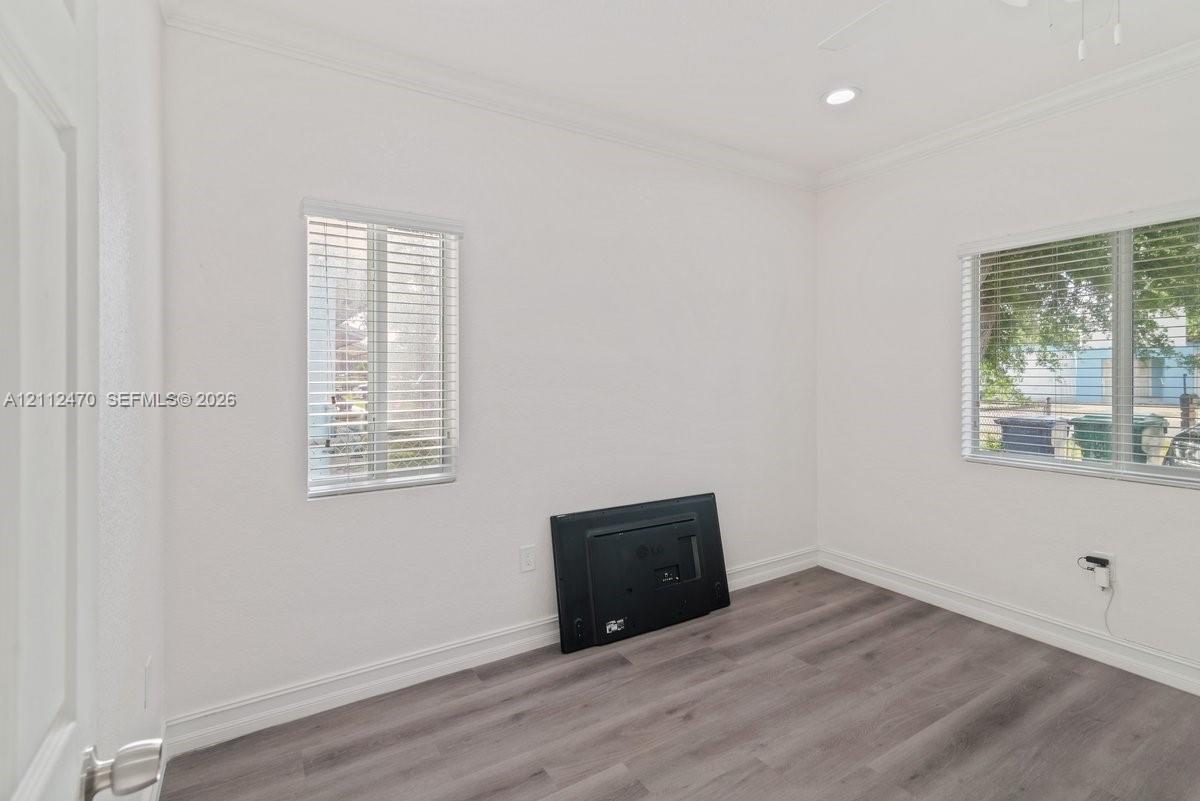 Neutral interior room featuring wood-finish flooring, crown molding, recessed lighting, and dual windows with horizontal blinds