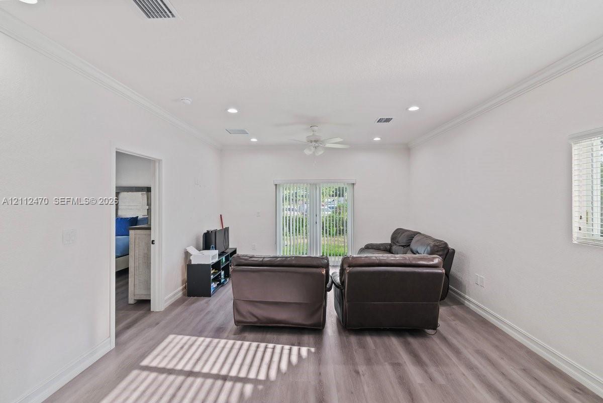 Living area featuring wood-finish flooring, recessed lighting, crown molding, a ceiling fan, and sliding glass doors with vertical blinds