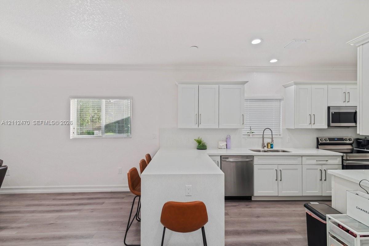 Kitchen featuring white cabinetry, solid-surface countertops, stainless steel appliances, and wood-finish flooring