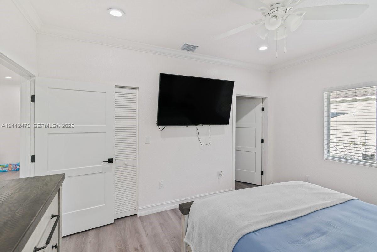 Room featuring recessed lighting, wood-finish flooring, crown molding, a ceiling fan, and louvered closet doors
