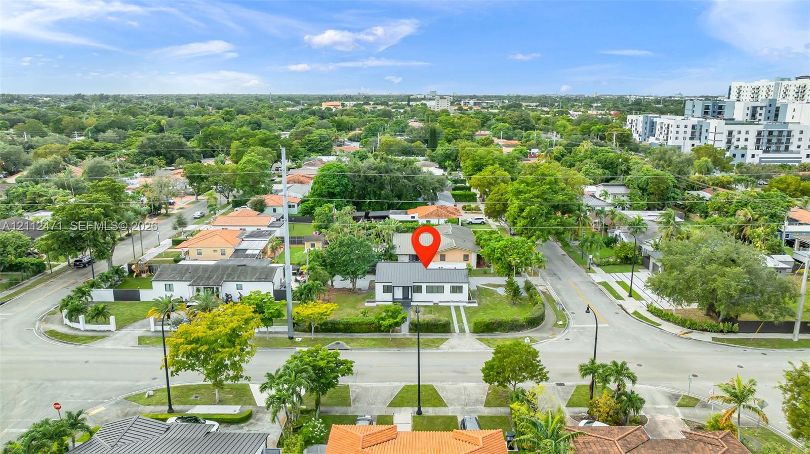 Aerial perspective of a detached single-story residence on a corner lot featuring a concrete driveway and mature perimeter landscaping
